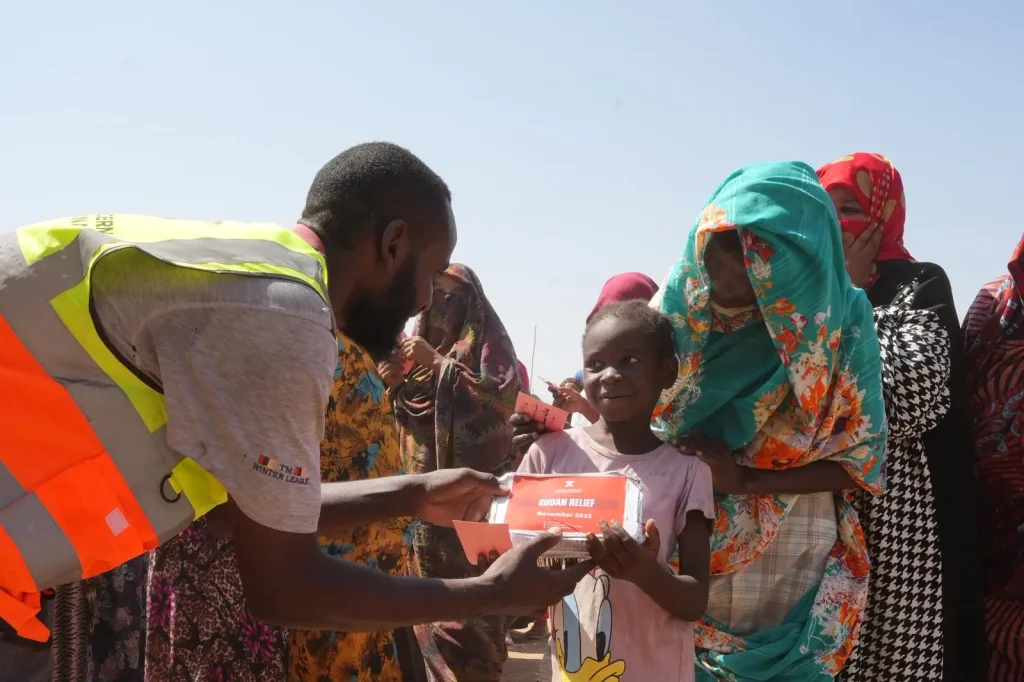 “Human Concern International volunteer handing a Sudan Relief food pack to a young girl during emergency aid distribution.